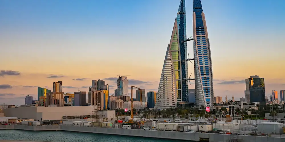 Bahrain World Trade Center's twin sail-shaped towers and wind turbines behind Manama's waterfront, under a pastel sky