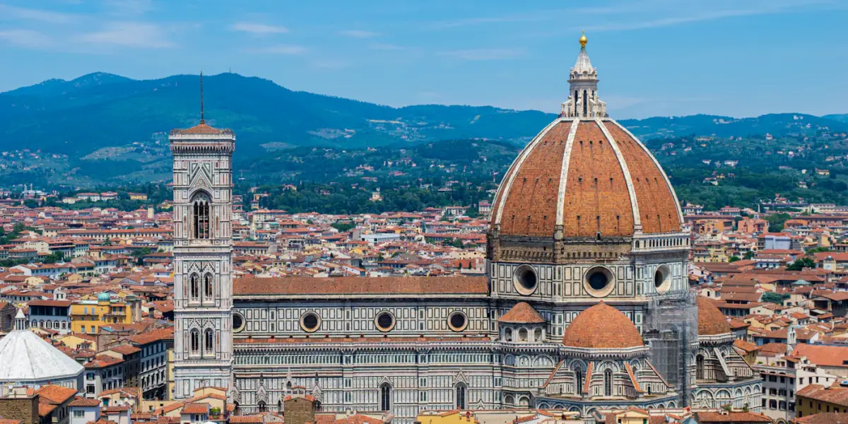 Florence Cathedral's red-brick dome and Giotto's marble bell tower above the city's terracotta rooftops, with green hills behind