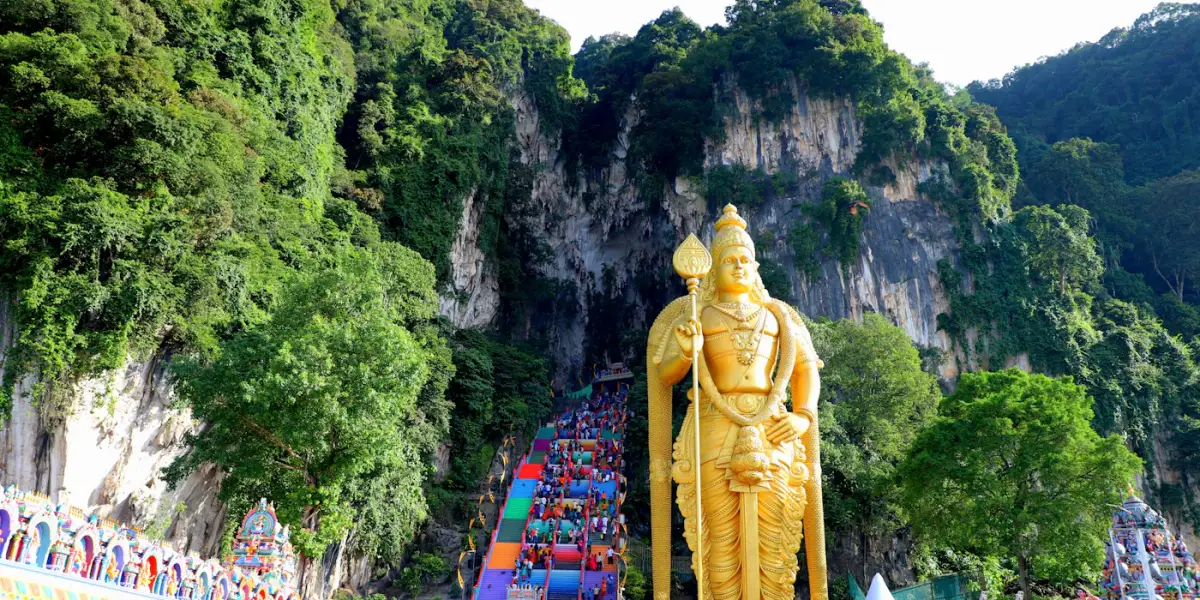 The golden Lord Murugan statue at Batu Caves beside the rainbow-painted steps up to the Temple Cave