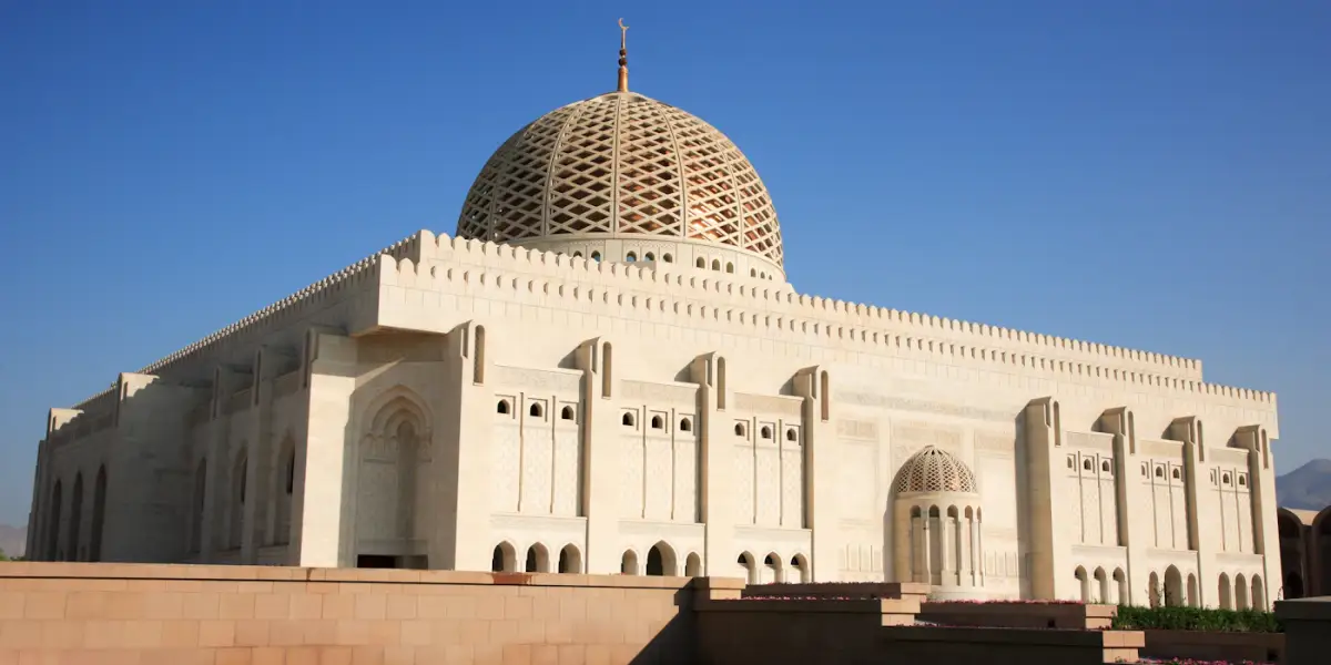 The Sultan Qaboos Grand Mosque in Muscat, its pale stone walls and latticed dome against a clear blue sky