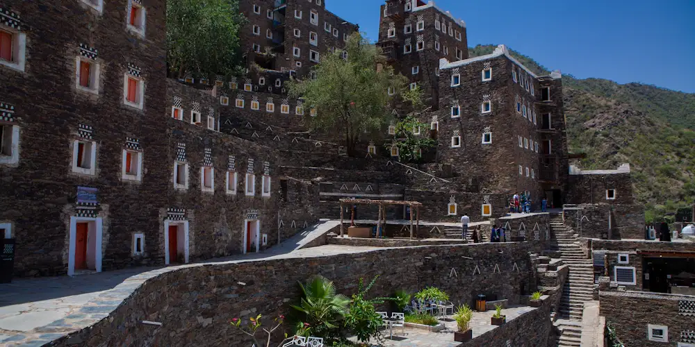 Stone tower houses with white-framed windows in the old village of Rijal Almaa, below green Asir hills