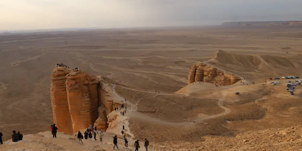 Visitors on the sheer sandstone cliffs of the Edge of the World above a vast desert plain