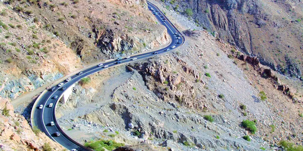 Cars on a road curving across a steep, rocky mountainside near Taif