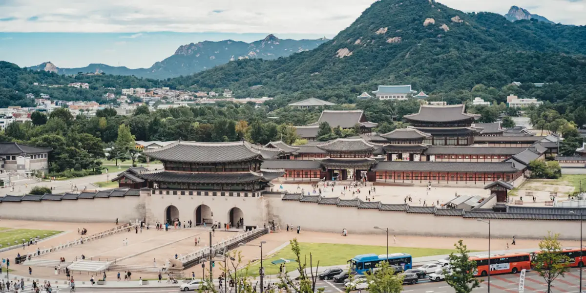 Gwanghwamun gate and the tiled halls of Gyeongbokgung Palace in Seoul, with forested mountains and rocky peaks rising behind