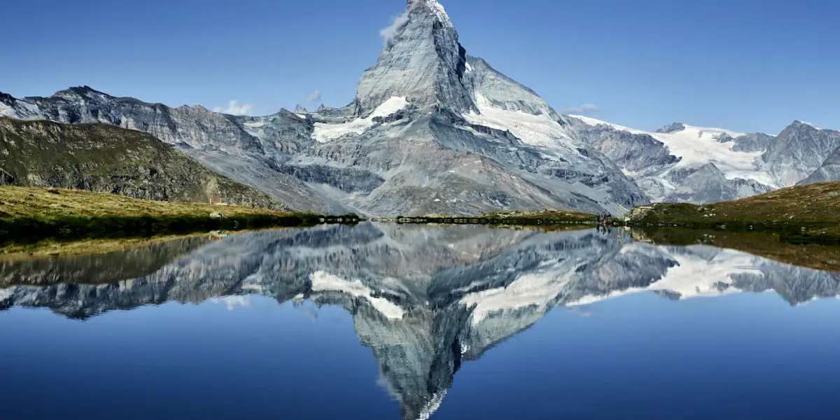The snow-streaked pyramid of the Matterhorn above Zermatt, mirrored in a still alpine lake under a clear blue sky