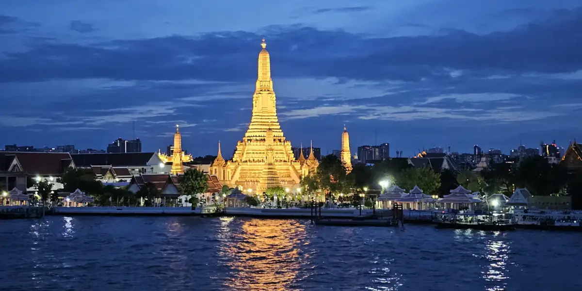 Wat Arun lit up at dusk, seen across the Chao Phraya River in Bangkok